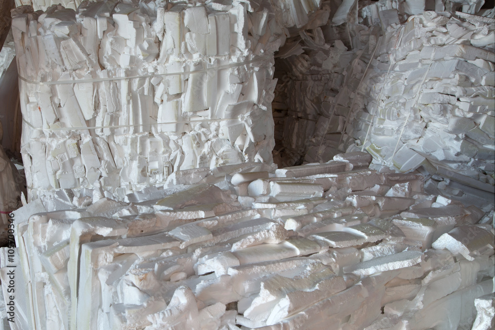 Large stacks of compacted white polystyrene foam blocks are piled together, creating a textured and irregular surface in an industrial styrofoam recycling facility. These blocks have been processed using high-quality densifiers, such as those from Better Densifiers, to ensure efficient and sustainable recycling.