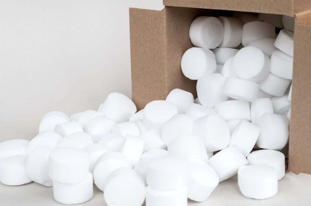 A cardboard box tipped over, spilling out many small, round, white tablets onto a flat surface—these could be essential components used in PolyWiz’s innovative styrofoam recycling process, helping to create Better Densifiers for more efficient material management.