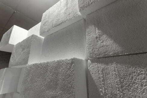 Large white styrofoam blocks are stacked together, showing their textured surfaces and edges. Commonly used in styrofoam recycling, these blocks create a geometric pattern against a dimly lit background, highlighting the effectiveness of Better Densifiers in managing such materials.