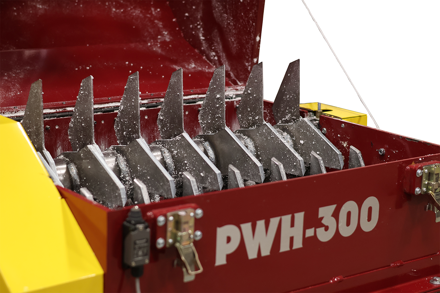 Close-up of a red and yellow industrial machine labeled PWH-300, known as the PolyWiz, with sharp metal blades inside, used for processing or shredding materials such as styrofoam for recycling purposes. White powder or residue is visible on the blades.