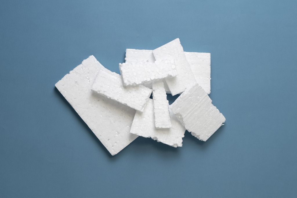 Several white rectangular pieces of styrofoam are arranged in a loose pile on a blue background, highlighting the need for innovative styrofoam recycling solutions such as those offered by Better Densifiers.