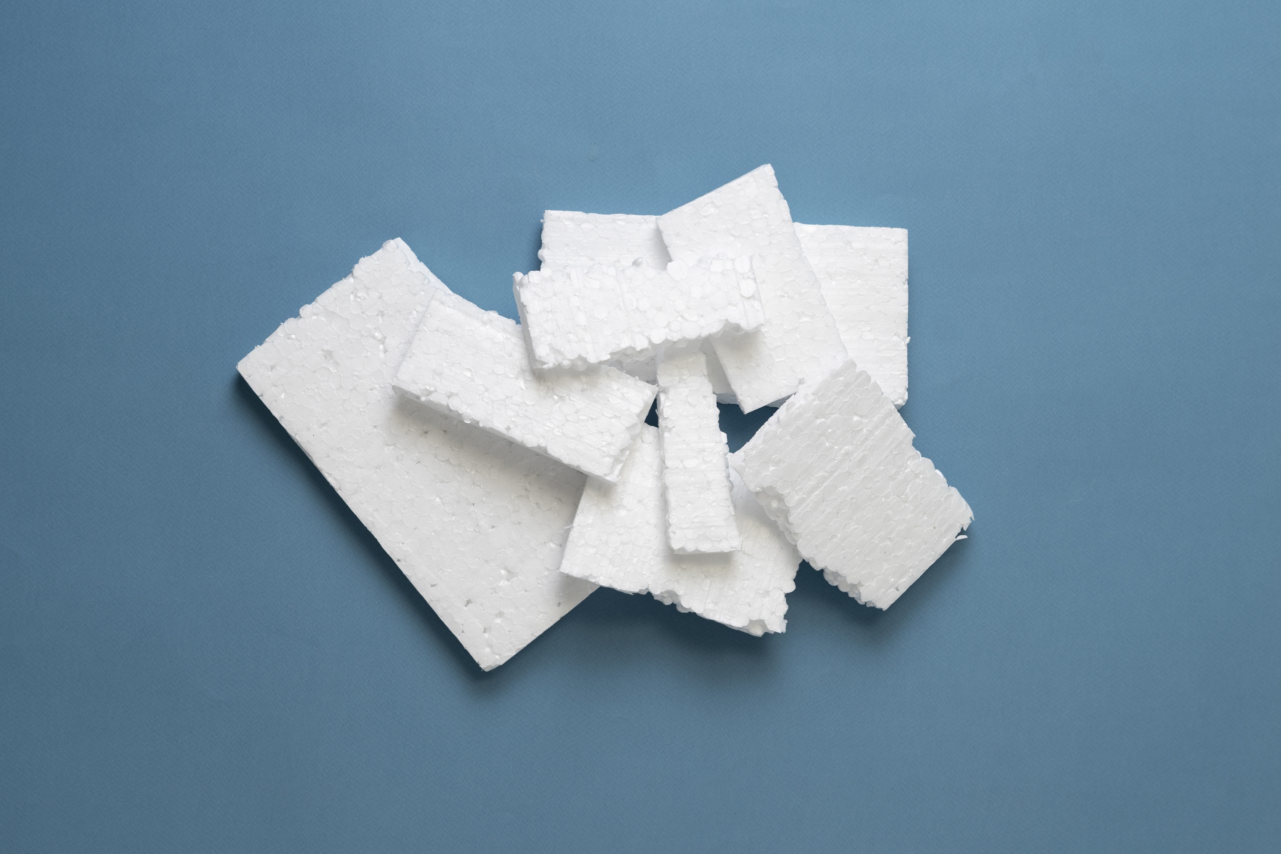Several white rectangular pieces of styrofoam are arranged in a loose pile on a blue background, highlighting the need for innovative styrofoam recycling solutions such as those offered by Better Densifiers.