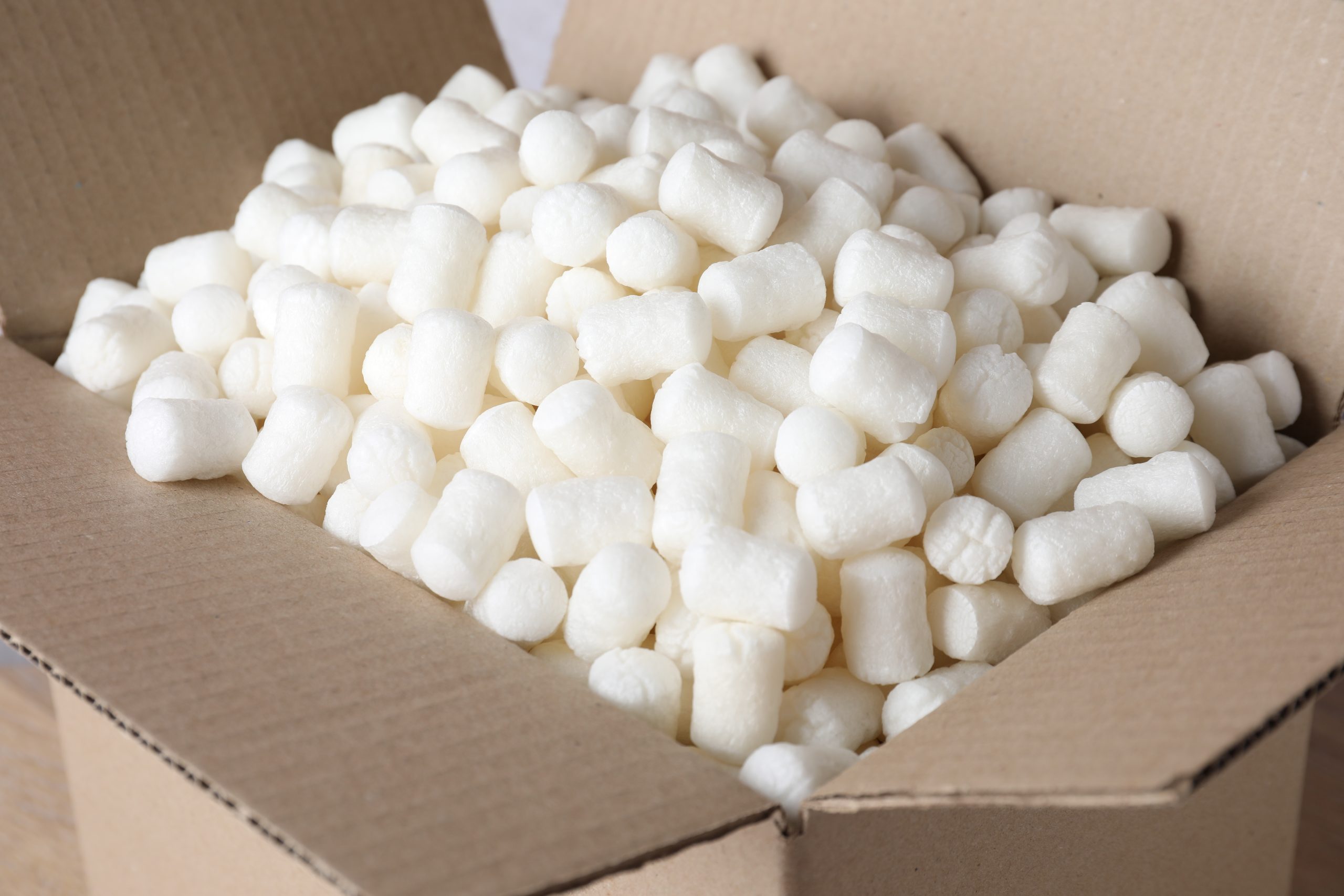 An open cardboard box filled with white, cylindrical packing peanuts—such as those produced by Better Densifiers—used for cushioning items during shipping.